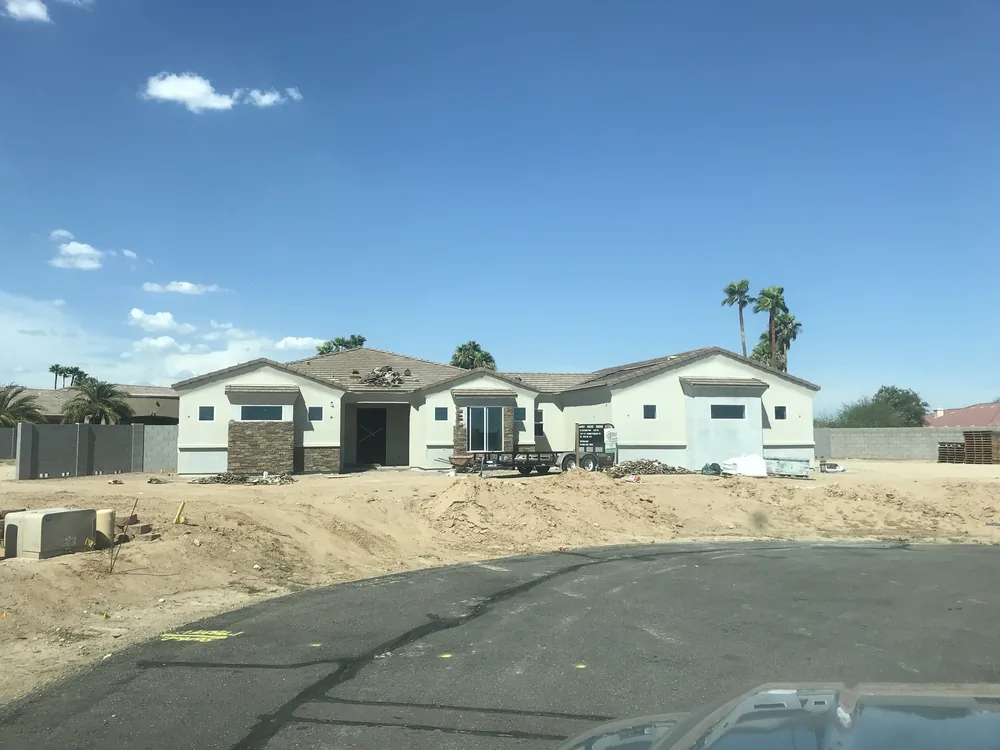 Stucco and stone home with exterior work progressing beyond a driveway