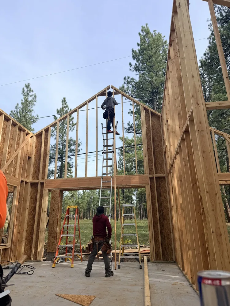 Crew working on the tall wall framing of a home among pine trees