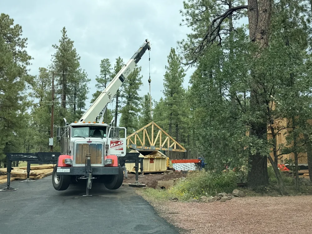 A crane unloading roof trusses at a pine forest construction site